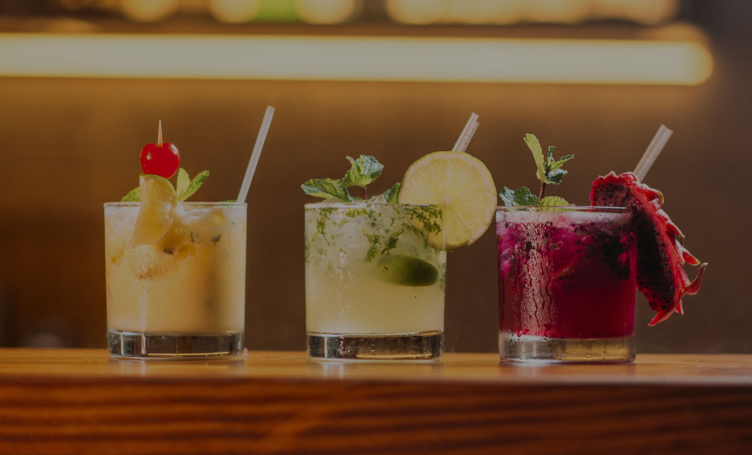 Three cocktails with mint, lime and fruit garnishes on a bar counter