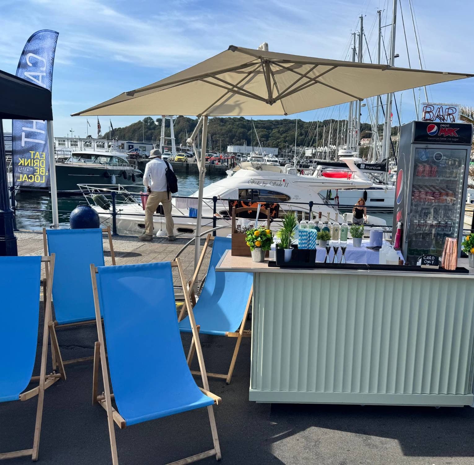 The Dirty Olive mobile bar with blue deckchairs and a parasol on a Guernsey harbour front